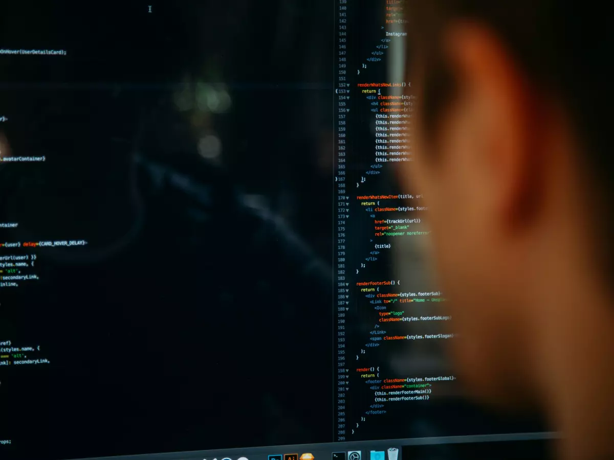 A person is sitting in front of a computer screen. The screen is showing code. The person is looking at the screen. The room is dark.