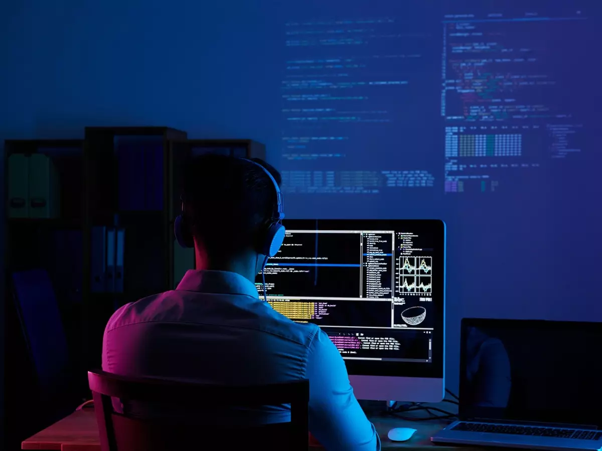 A man with headphones is sitting in front of a computer with code on the screen.