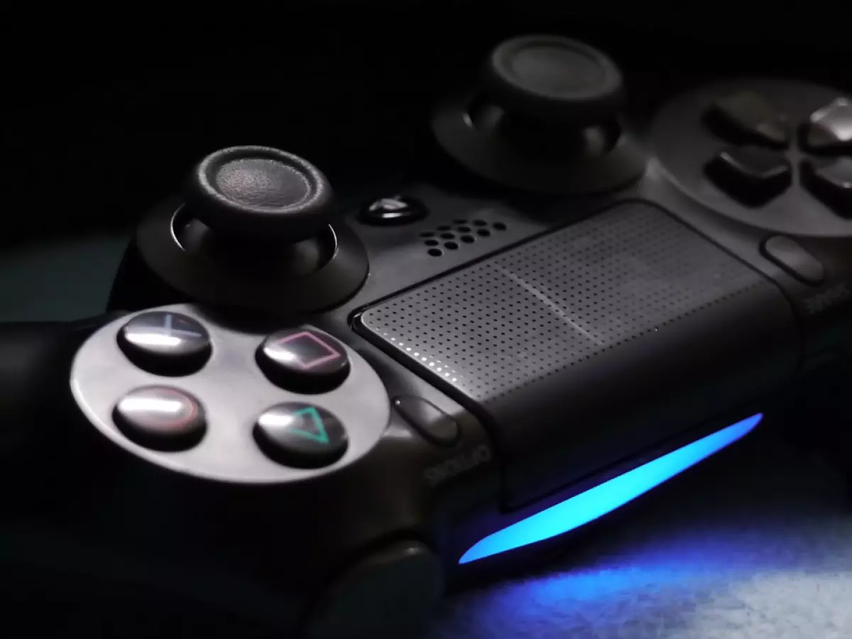 Close-up image of a black PS4 controller, with a blue light bar glowing, on a blue background.