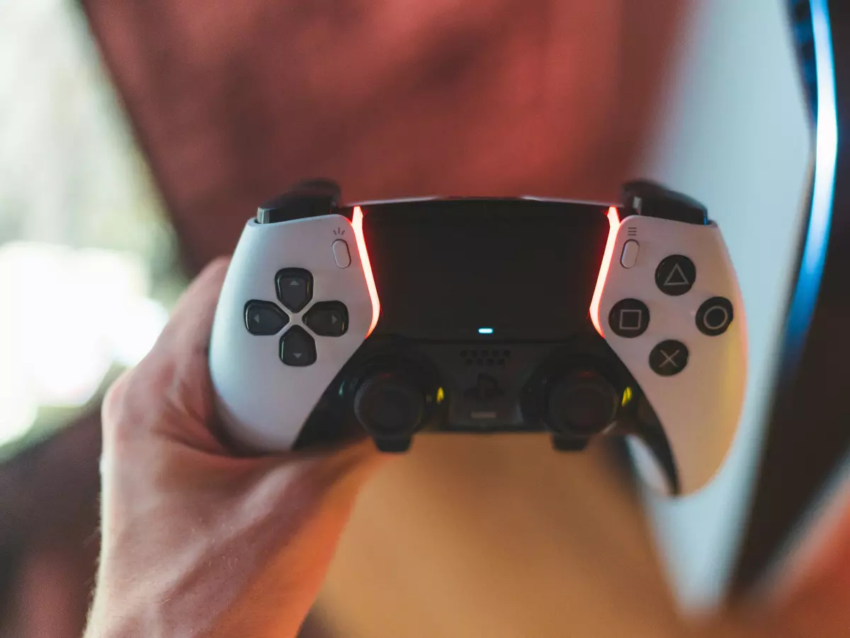 A person holds a white PlayStation DualSense Edge controller in their hand, with the focus on the controller's buttons and features.