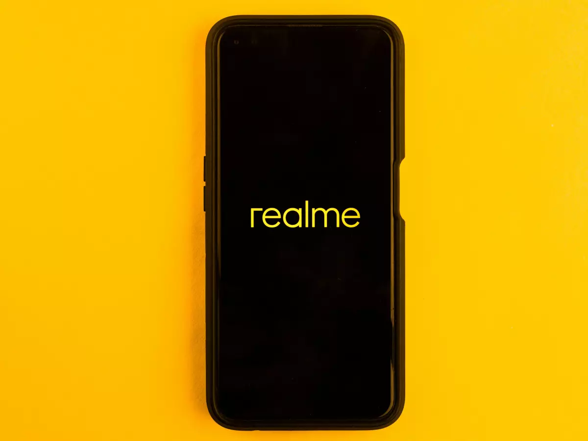 A Realme phone is displayed on a yellow background, showcasing the phone's front and the Realme branding.