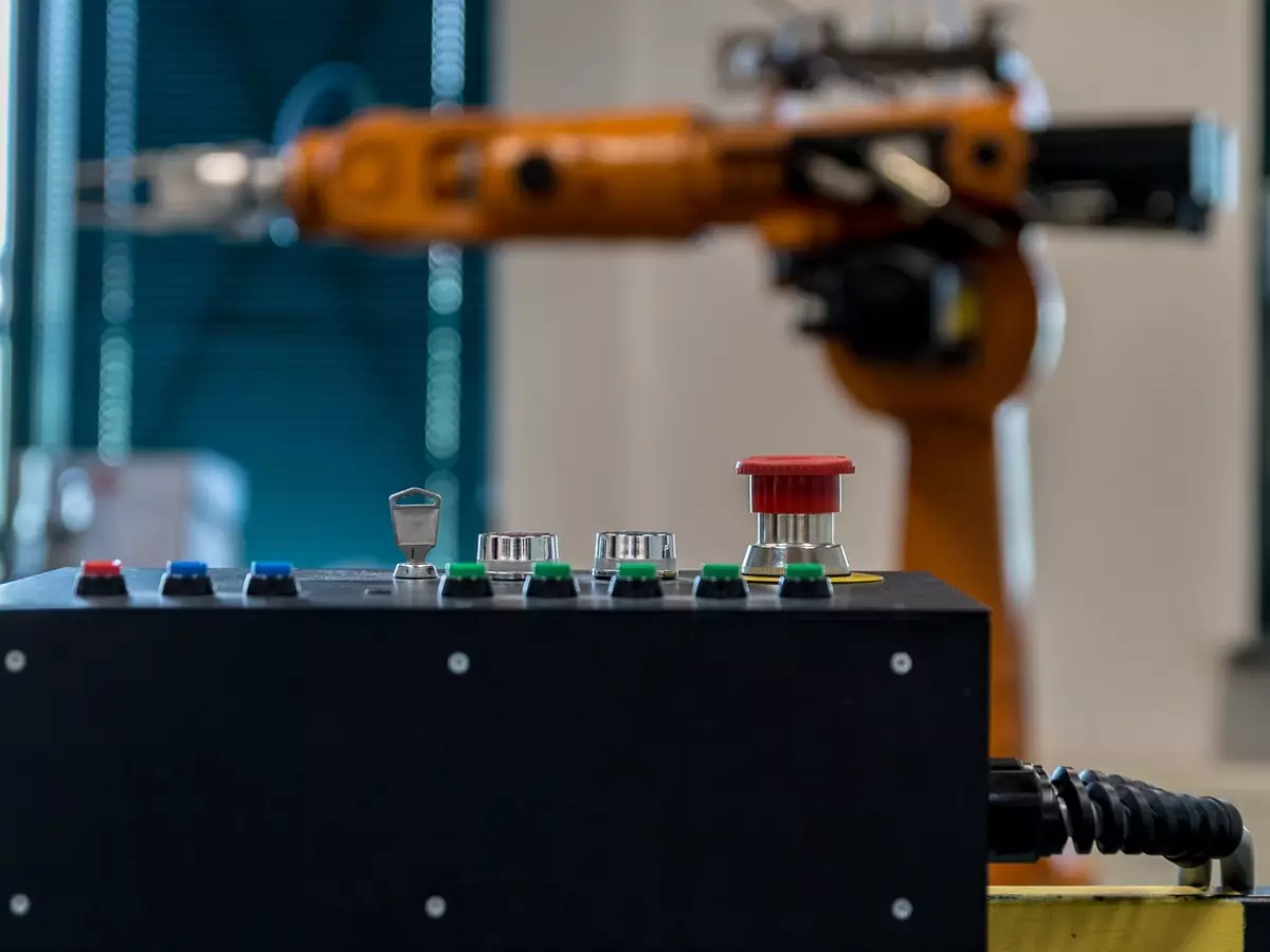 Close-up of a control panel with a red button, with a robotic arm in the background