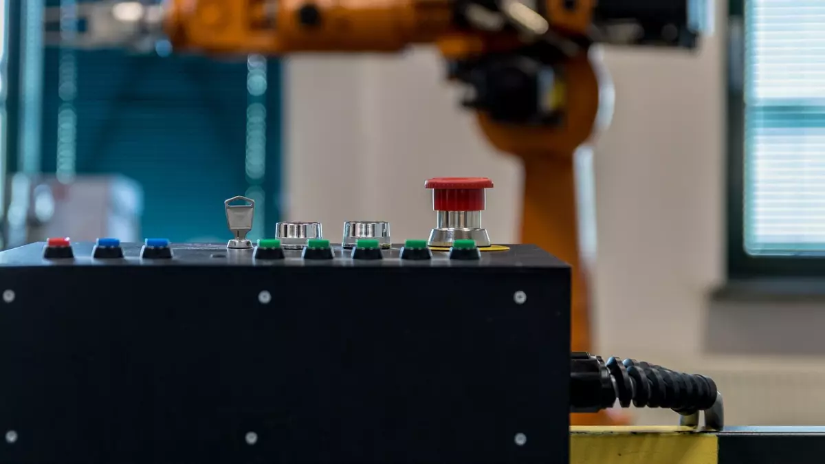 Close-up of a control panel with a red button, with a robotic arm in the background