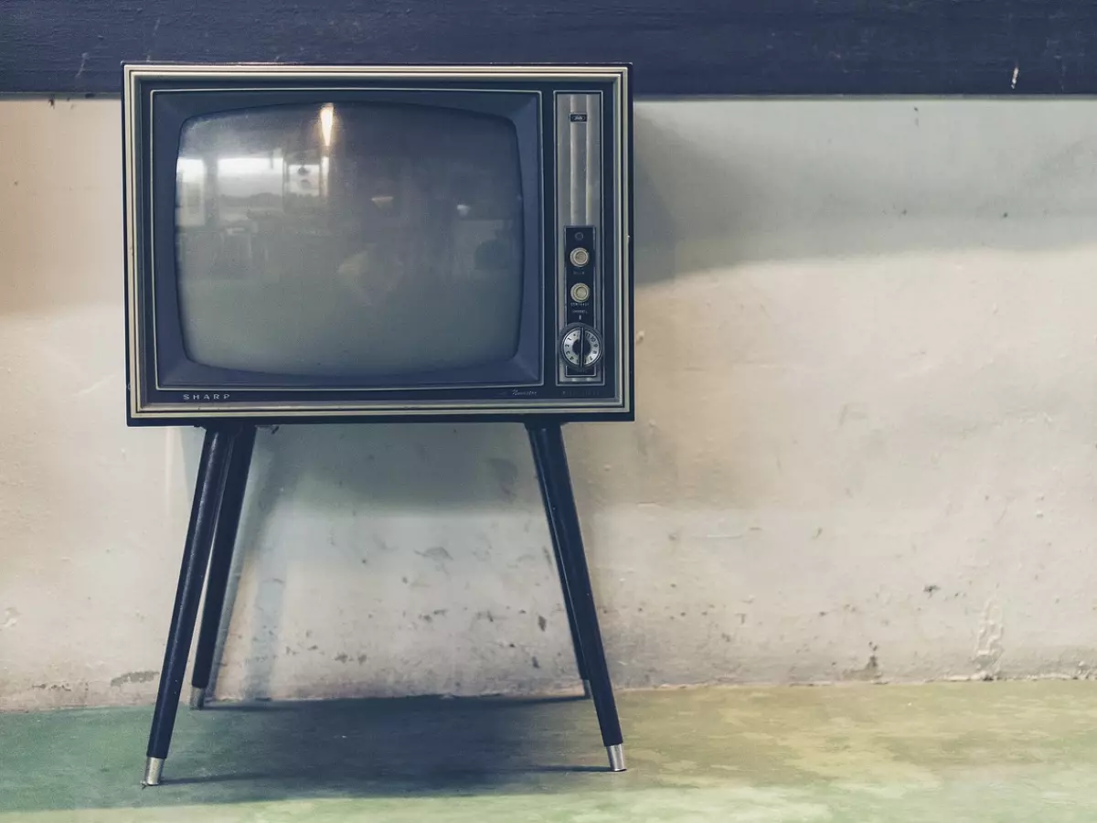 A vintage television set on a stand, facing a white wall. The television is turned off, showing a dark screen. 