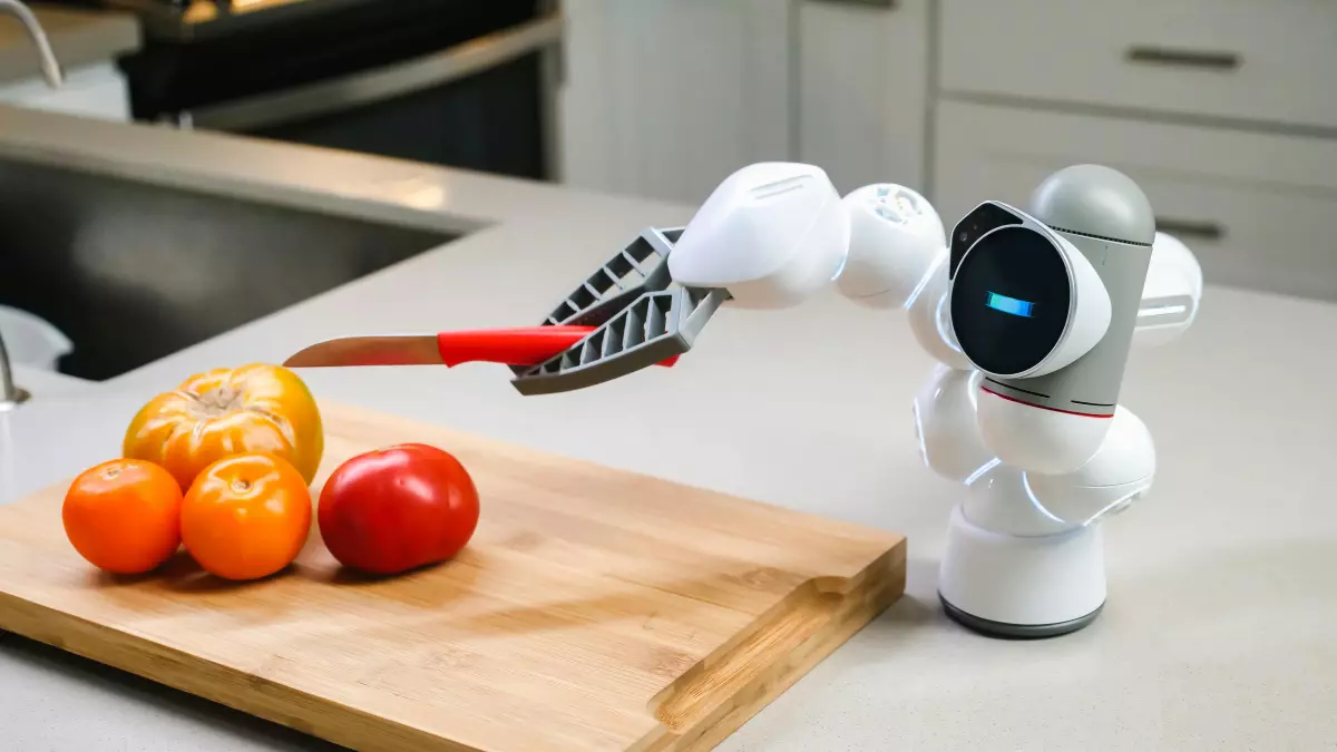 A white robot arm with a knife cuts a tomato on a wooden cutting board.