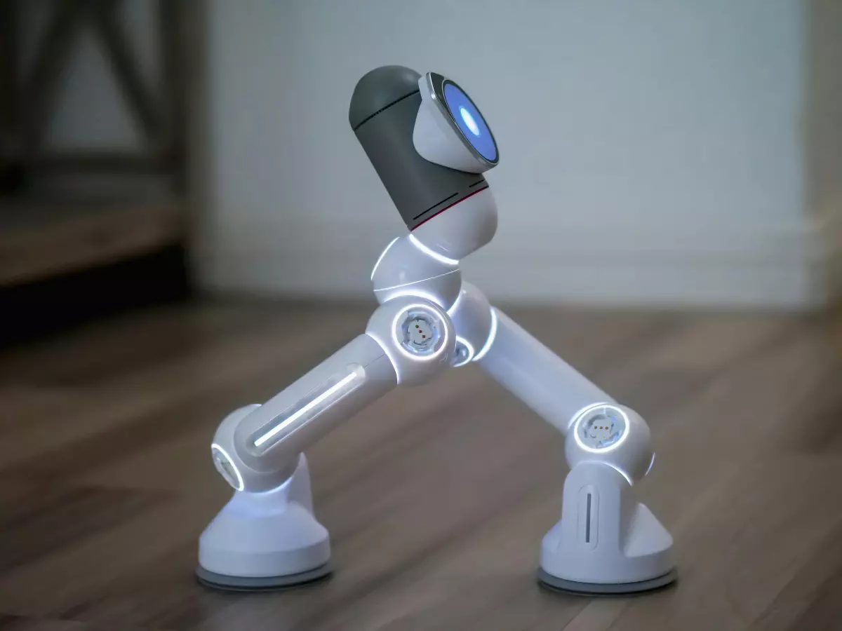 A white humanoid robot with three legs walks on a wooden floor. The robot has a round head with a blue light.