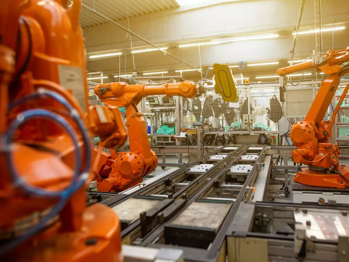 Two orange robotic arms work together on an assembly line in a factory.