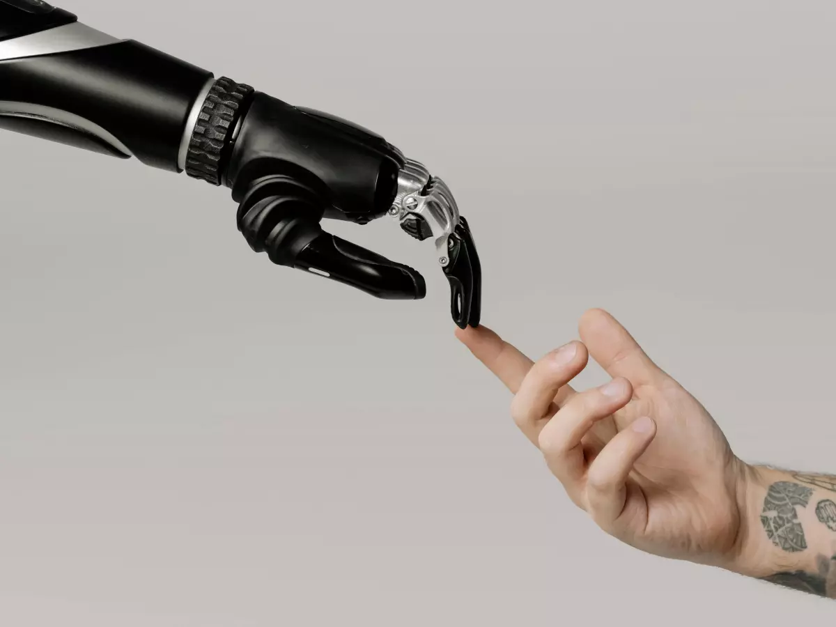 A robotic hand, silver and black, reaches out to touch a human hand with a tattoo. 