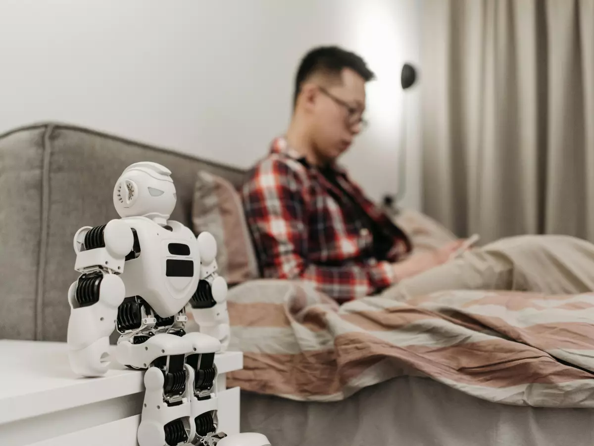 A man is sitting on a couch in a living room. A robot is standing next to him.