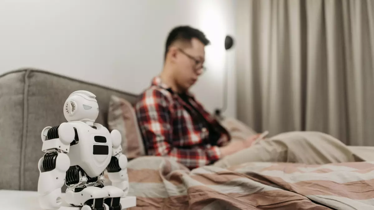 A man is sitting on a couch in a living room. A robot is standing next to him.