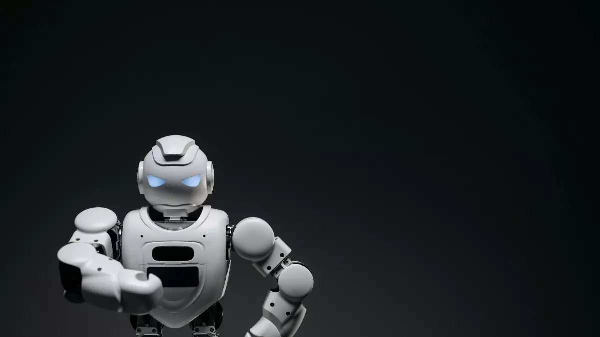 A humanoid robot with white and grey body and blue eyes standing on a dark background with one arm raised.