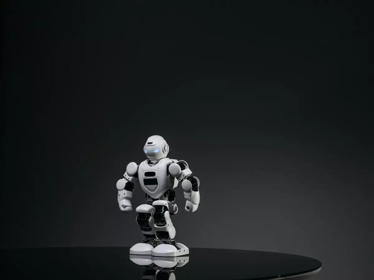 A white humanoid robot with black joints, standing on a circular platform.