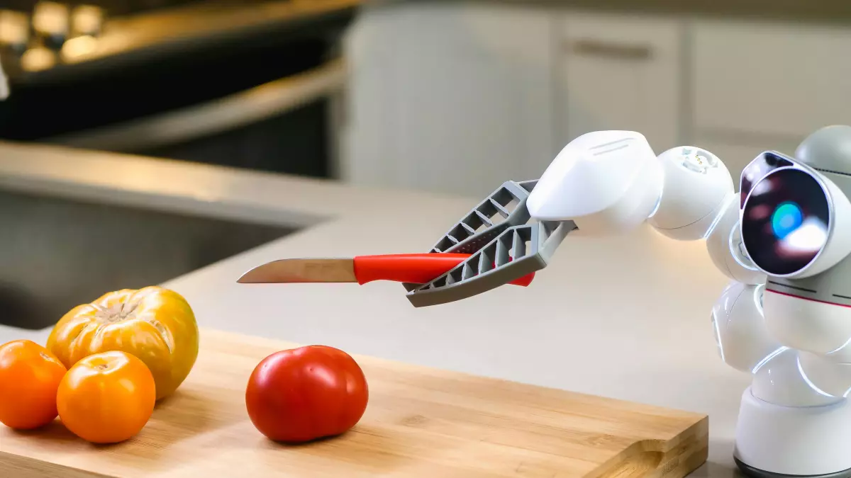 A white humanoid robot with a robotic arm holding a knife on a wooden cutting board with a tomato and a few oranges nearby.