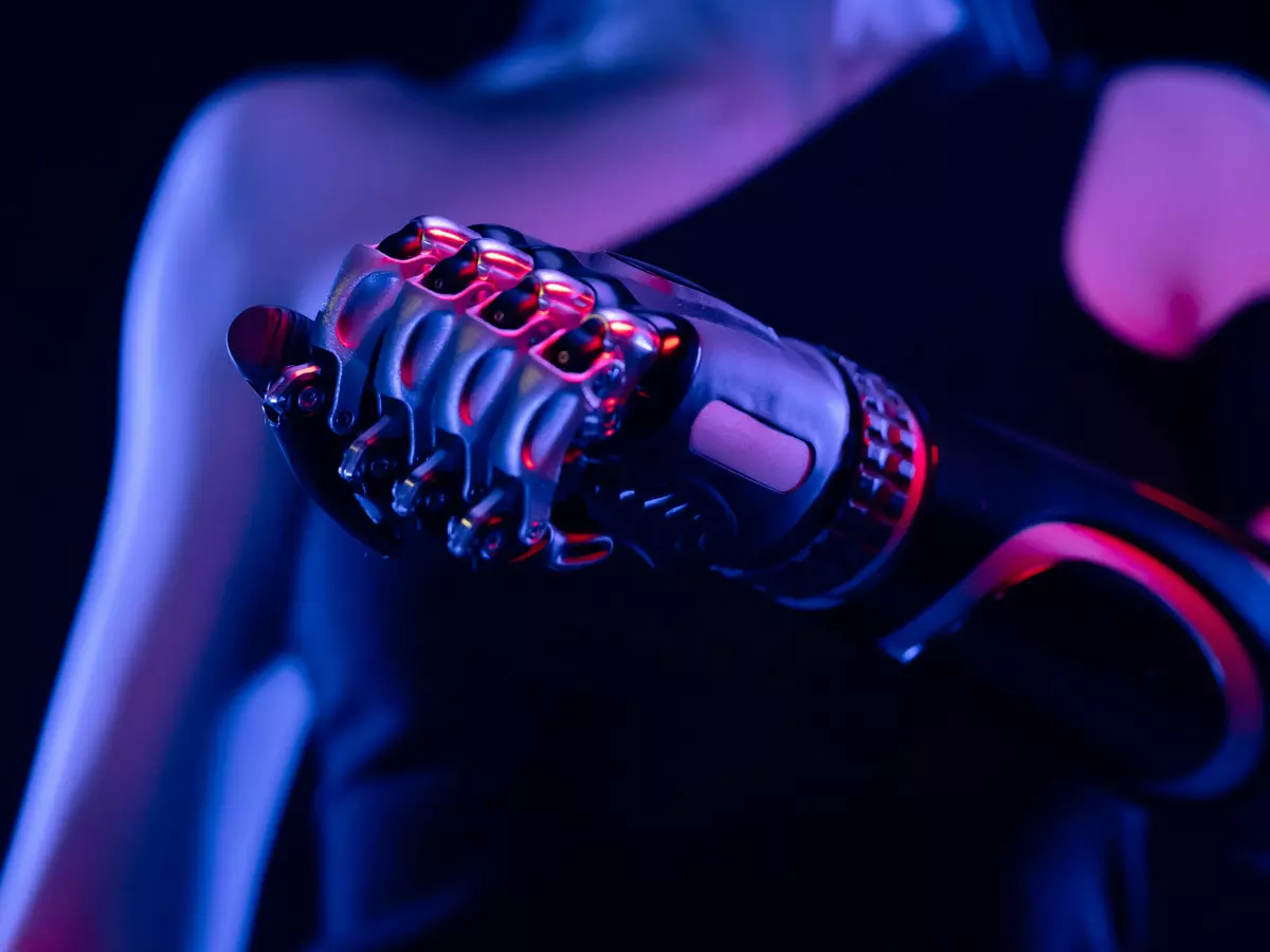 Close-up shot of a futuristic robotic arm or prosthetic, glowing with pink and blue neon light against a dark background.