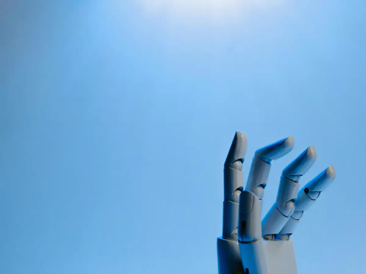 A robotic hand reaching up against a blue background, with a light source shining from above.