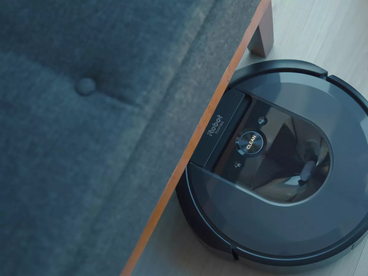 A close-up shot of a Roomba robot vacuum cleaner cleaning under a couch, showcasing its round shape and compact design, ideal for navigating tight spaces.