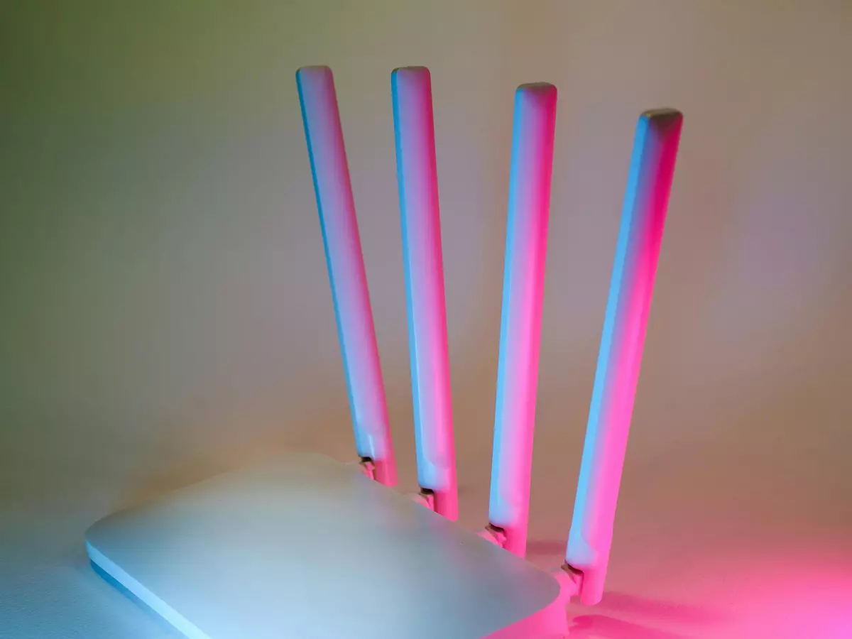 A white router with four antennas is sitting on a surface, illuminated by colored lights.