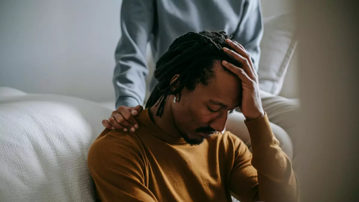 A person sitting on a couch with their head in their hands, looking distressed.