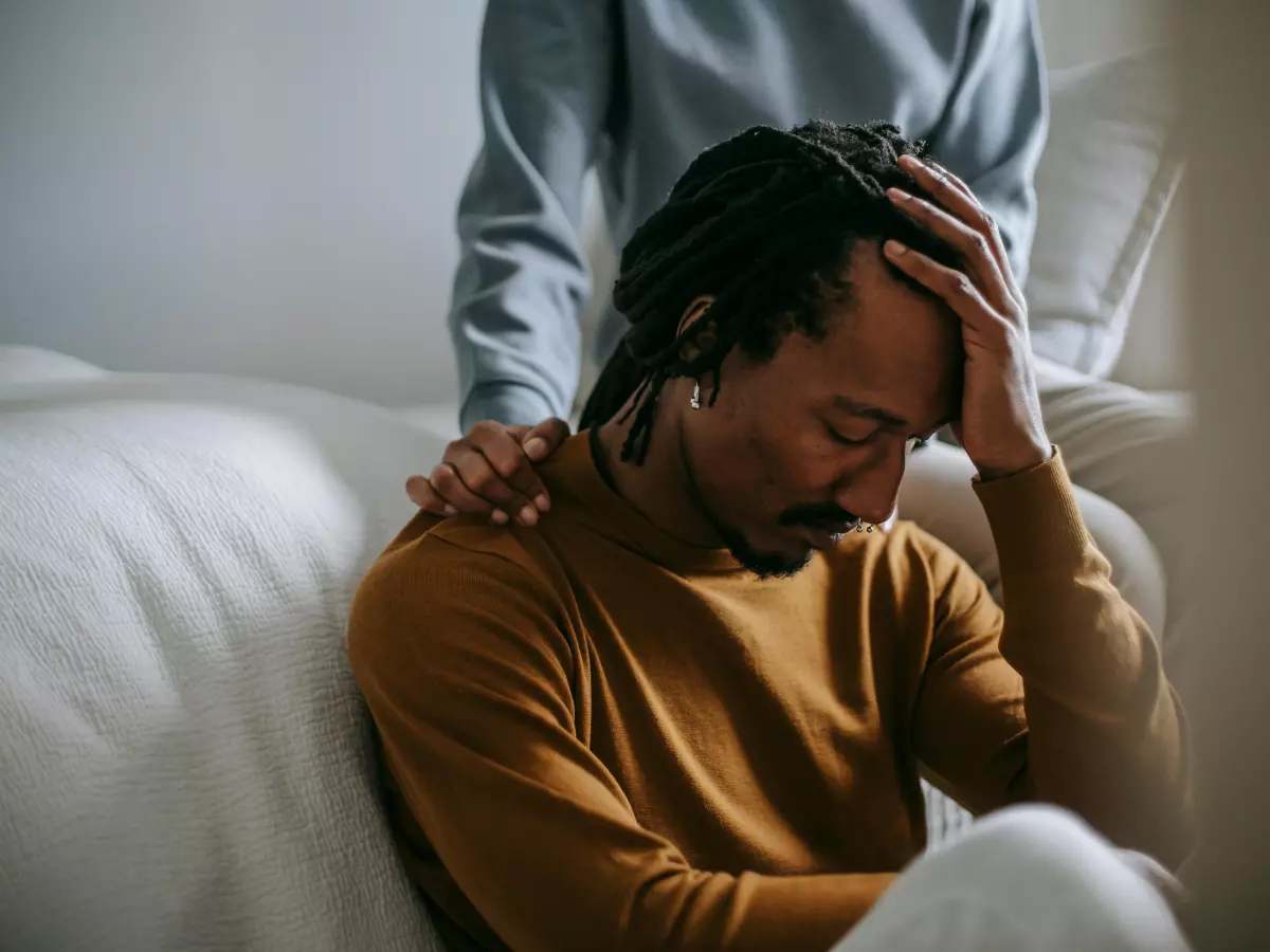 A person sitting on a couch with their head in their hands, looking distressed.