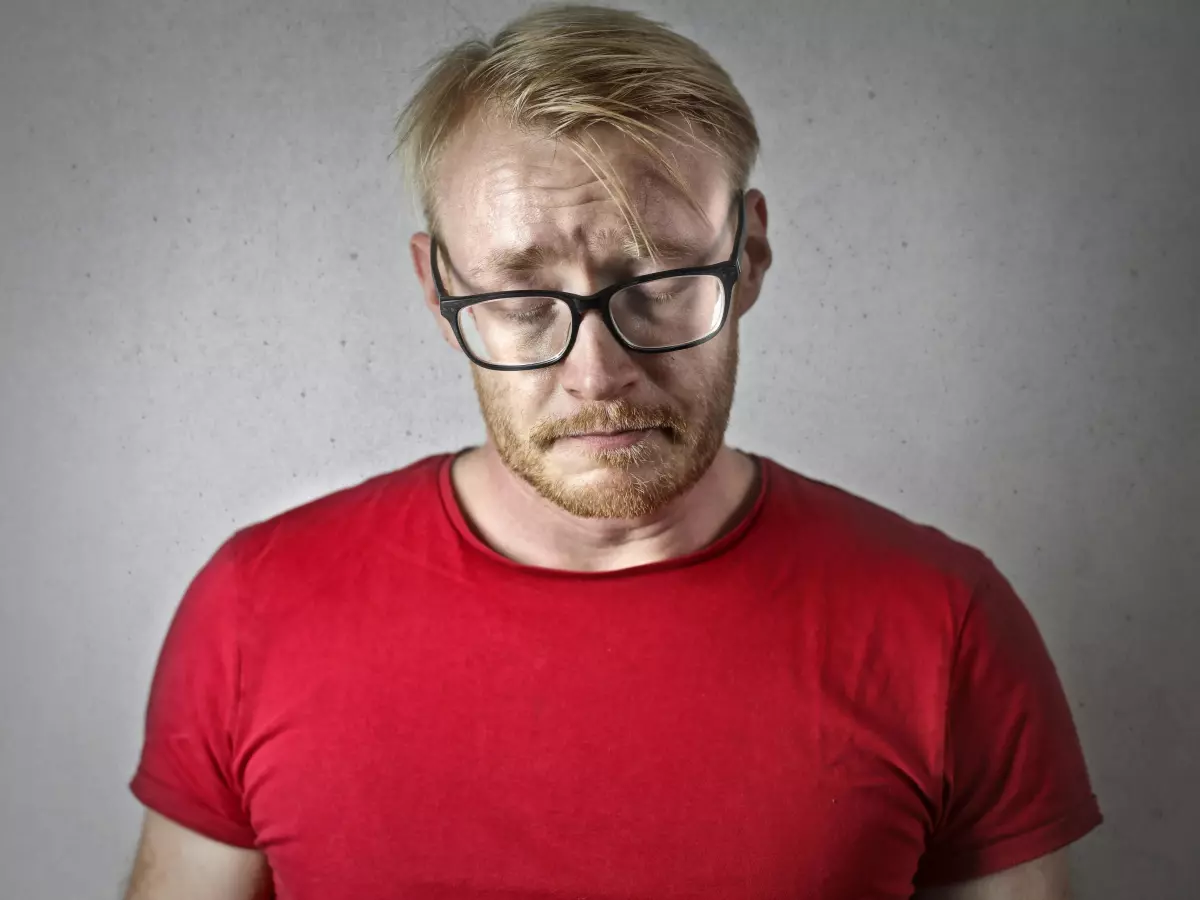 A man in a red shirt is looking down, appearing disappointed.