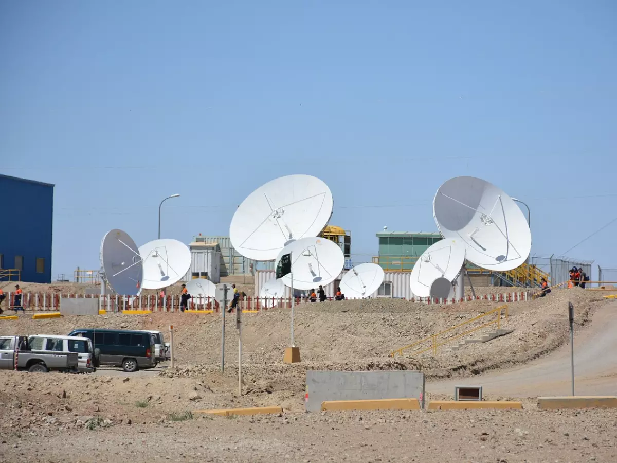 A ground station with several large satellite dishes. There are people working around the dishes and cars parked nearby. 