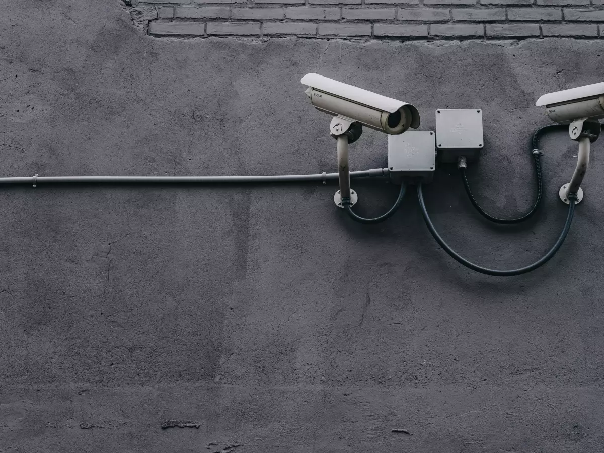 Two security cameras mounted on a wall, with wires and a box connecting them.