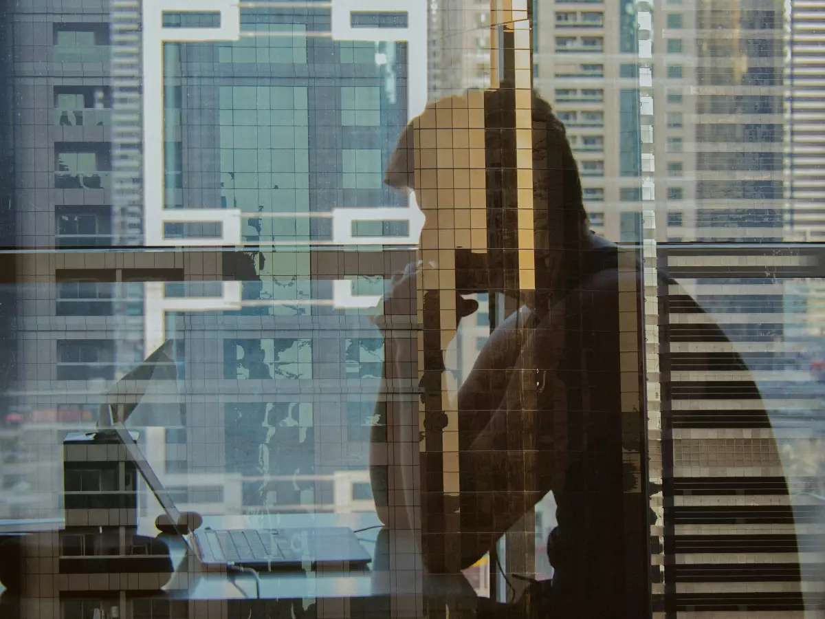 A silhouette of a person working on a laptop in front of a window with a city view.