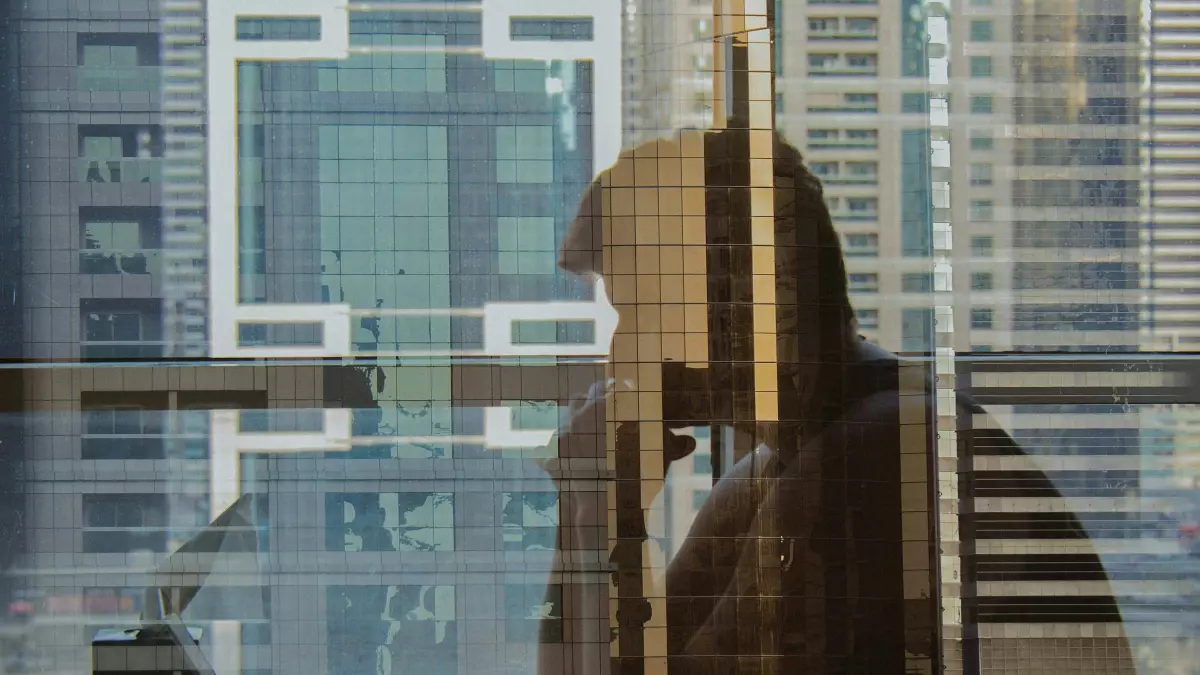 A silhouette of a person working on a laptop in front of a window with a city view.