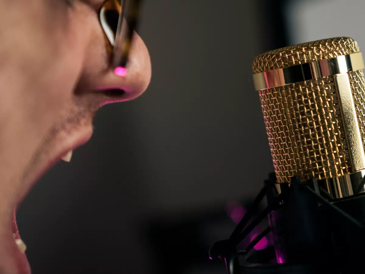 A person's mouth open with a microphone close up, showing the person's nose.