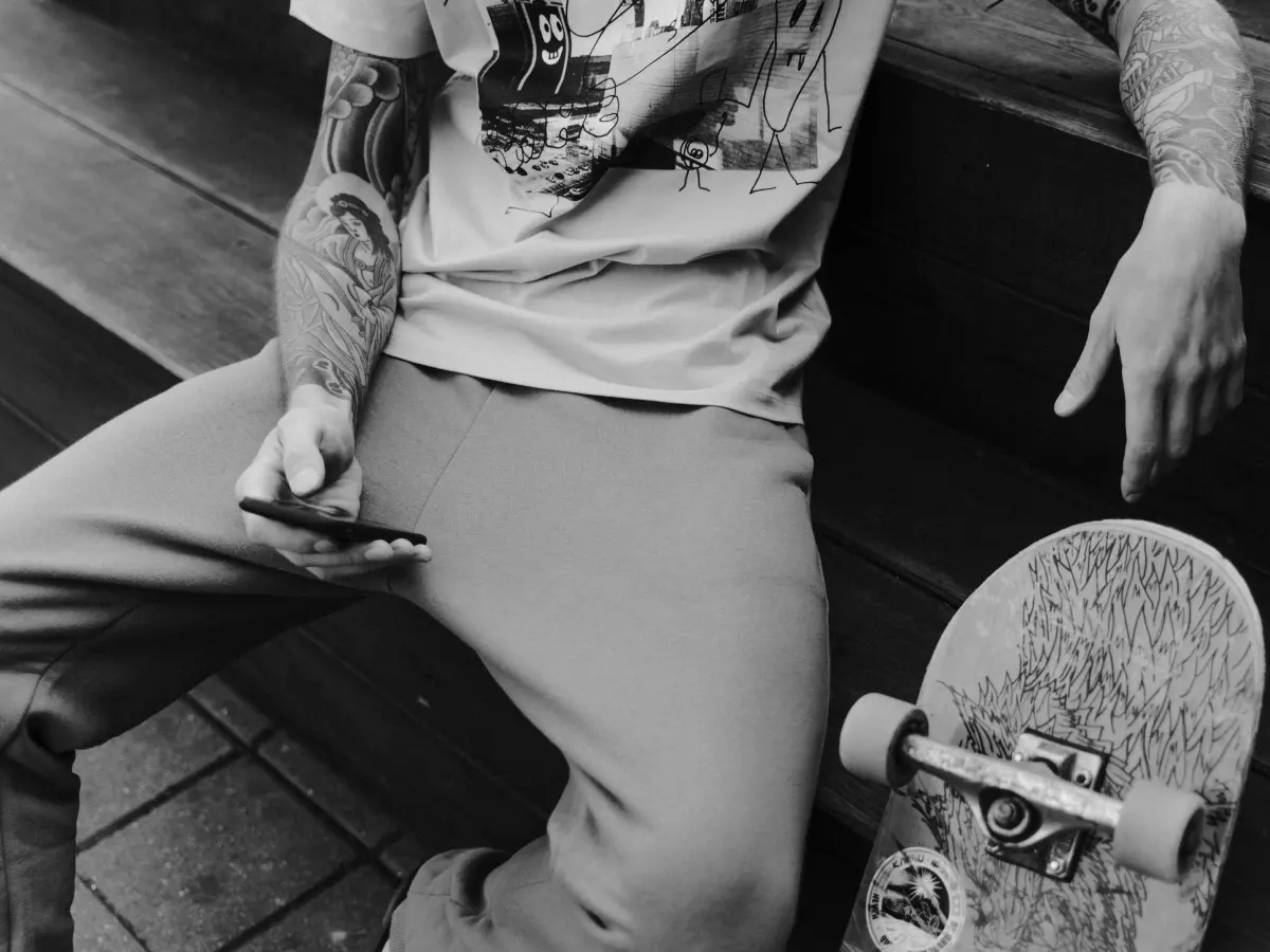 A man with tattoos is sitting on a bench holding a skateboard.