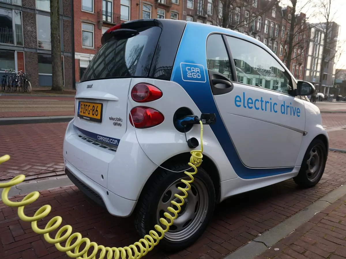 A white electric car is being charged with a yellow cable, the car has the sign electric drive on it.