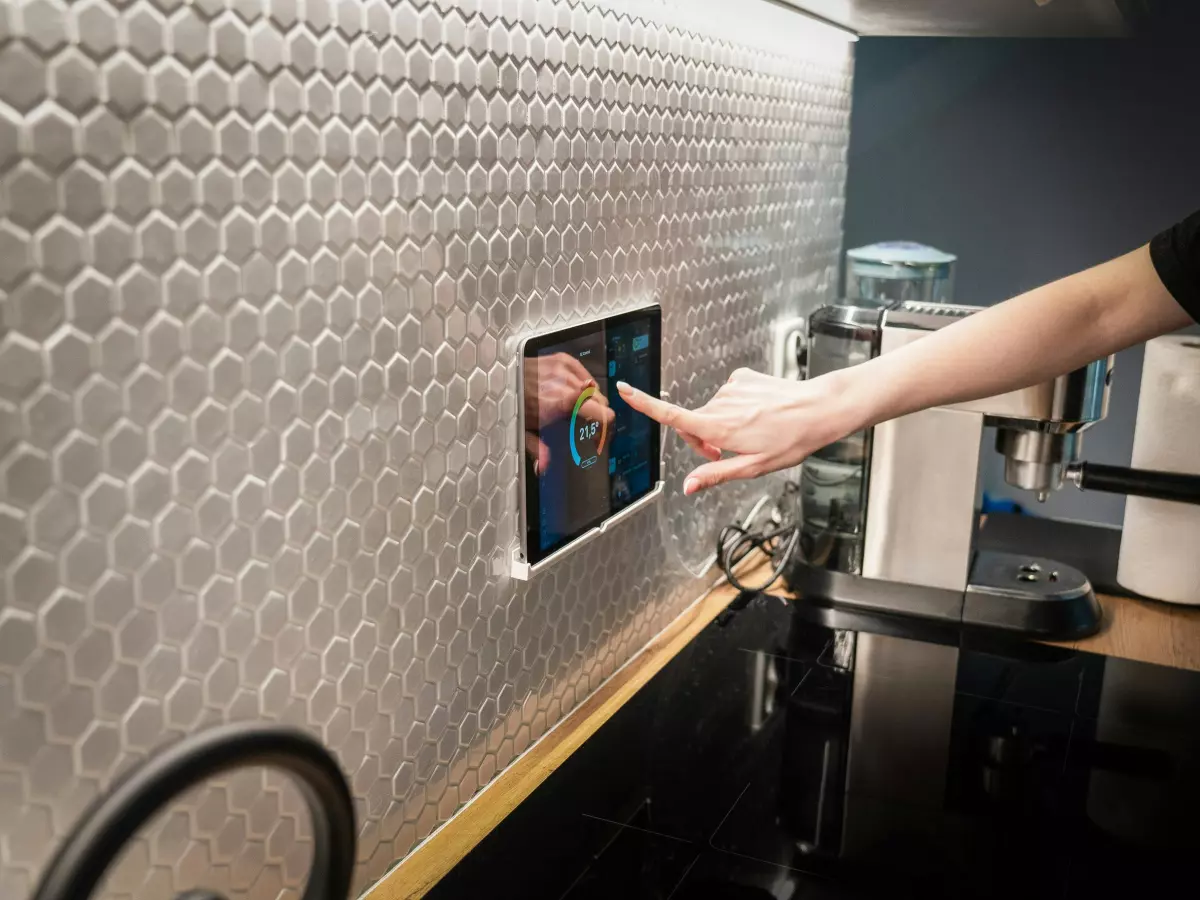 A person using a wall-mounted tablet to seemingly control smart home devices in a kitchen. This showcases the integration of technology into daily life.