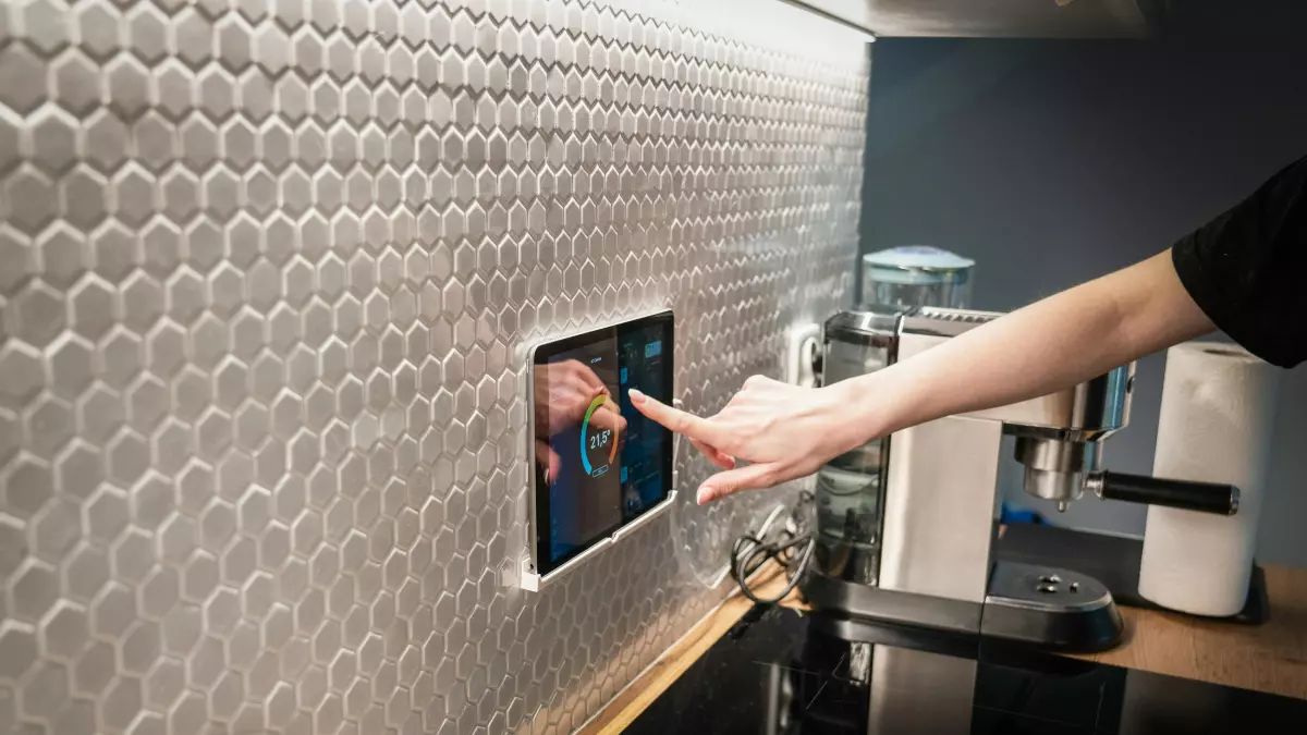 A person using a wall-mounted tablet to seemingly control smart home devices in a kitchen. This showcases the integration of technology into daily life.