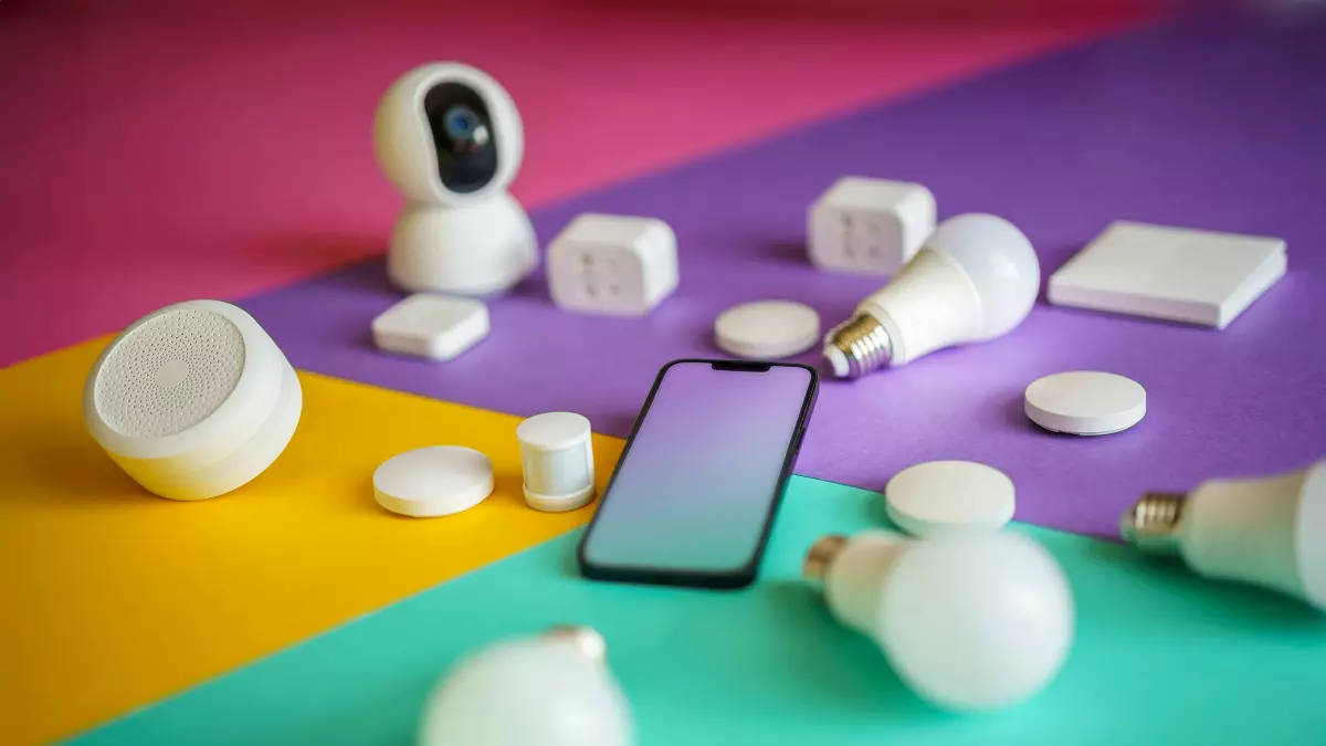 A flatlay of various smart home devices including a smartphone, security camera, smart lights, and smart plugs on a vibrant colored background.