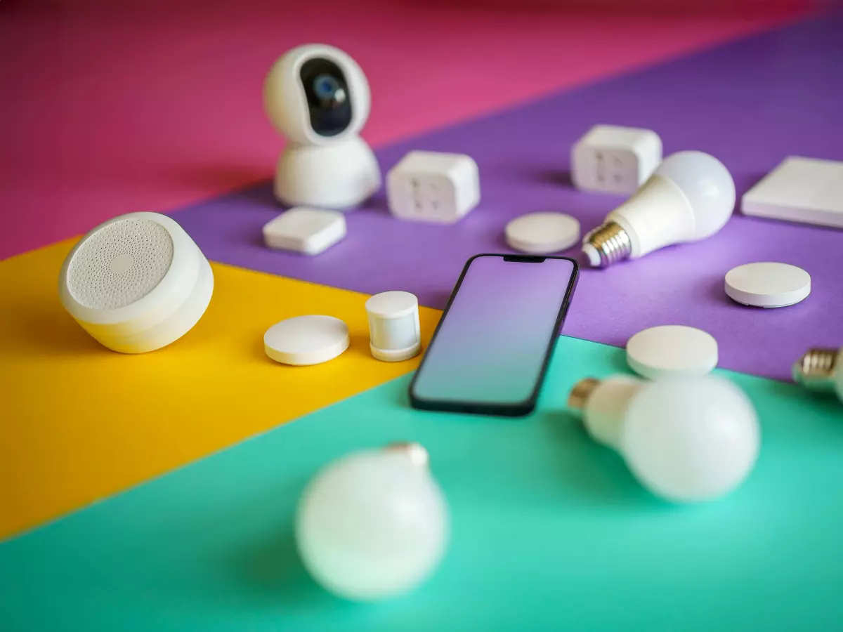 A flatlay of various smart home devices including a smartphone, security camera, smart lights, and smart plugs on a vibrant colored background.