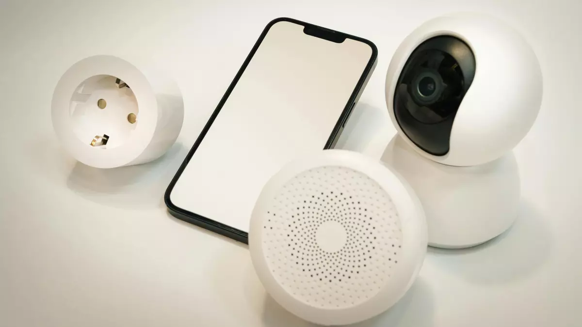 A smartphone lies at the center of the image, flanked by a smart security camera, a smart plug, and a smart speaker. All devices are white, creating a cohesive visual.