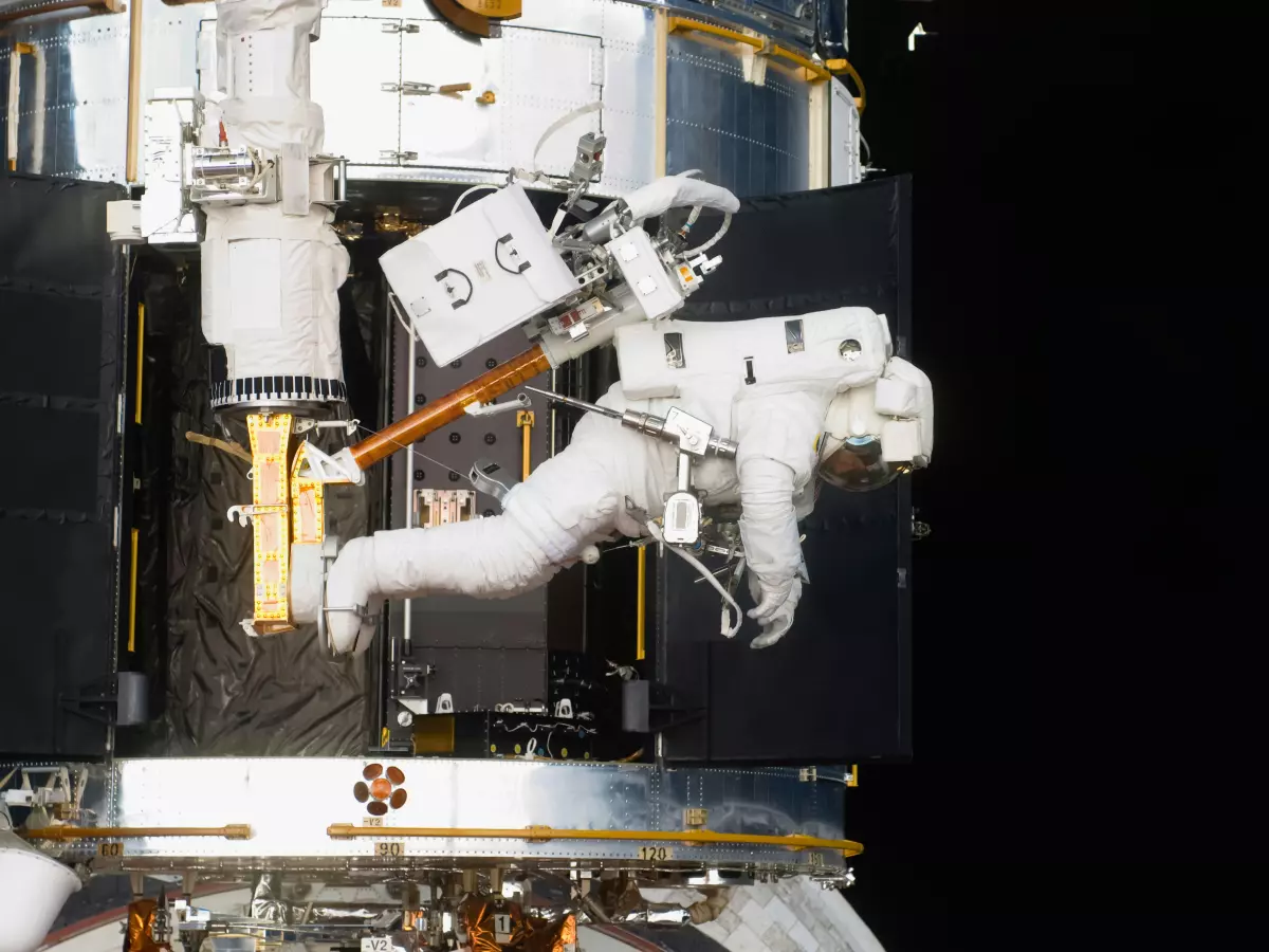 An astronaut working on a satellite in space, against a dark background.