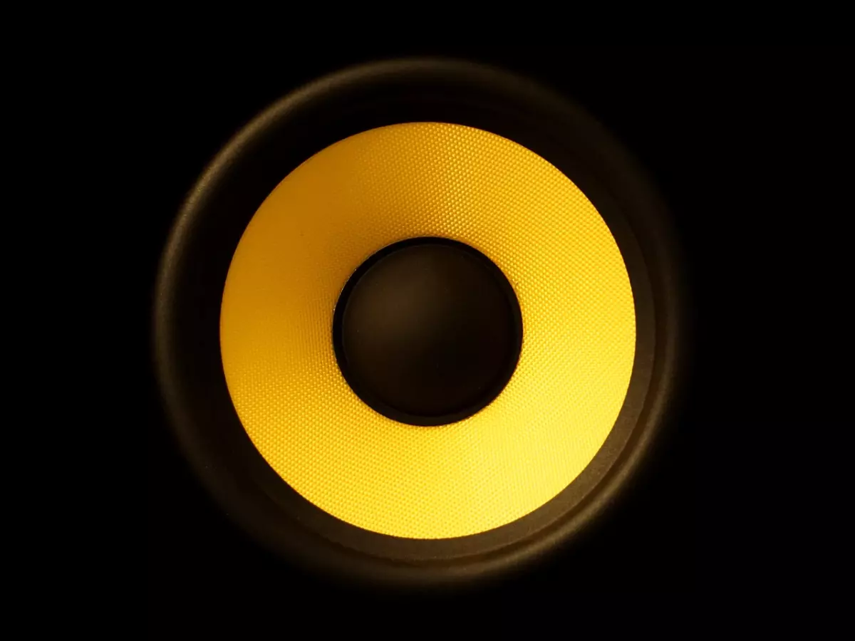 A close-up of a speaker, the yellow membrane and black grille stand out against a black background.