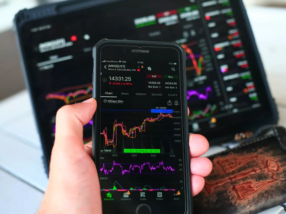 A person holding a smartphone showing a live stock chart with a line graph fluctuating rapidly.