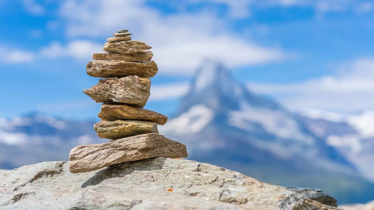 A stack of stones standing on a rocky surface, with a snowy mountain peak in the background.