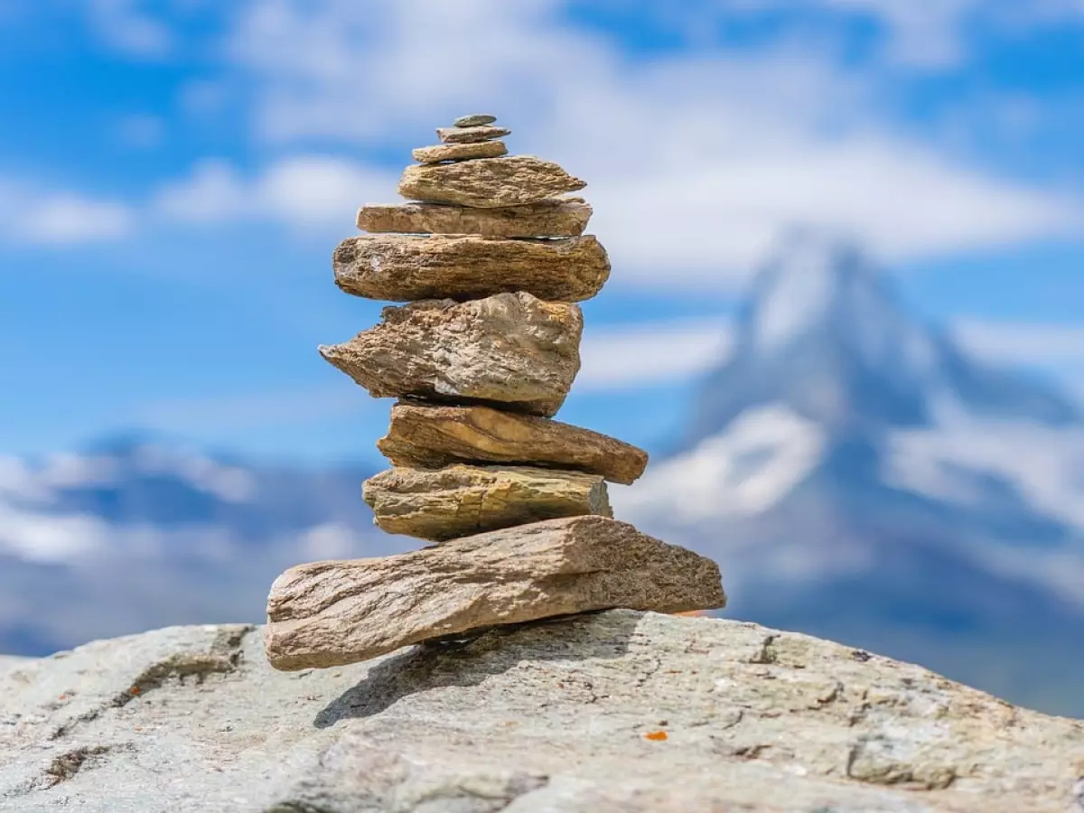 A stack of stones standing on a rocky surface, with a snowy mountain peak in the background.