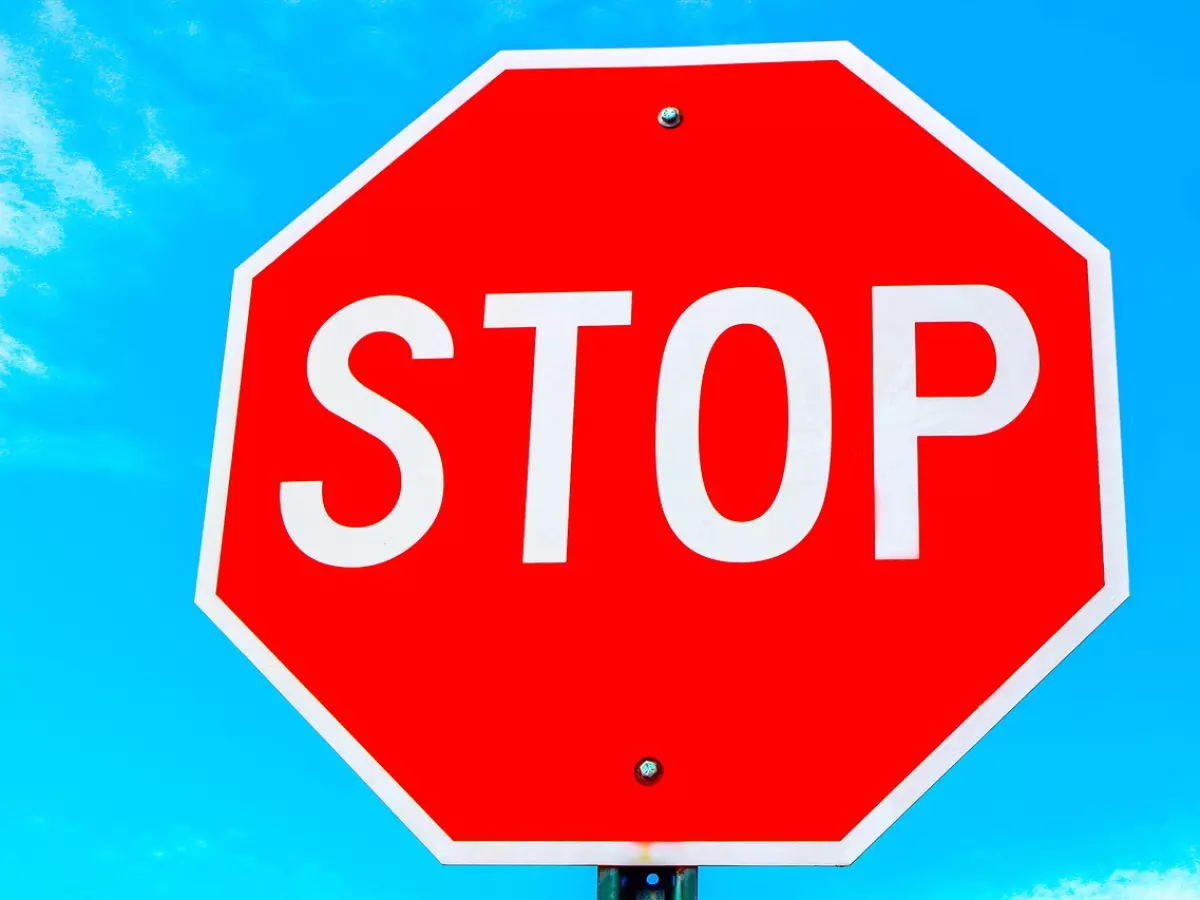 A red stop sign with white lettering against a blue sky.