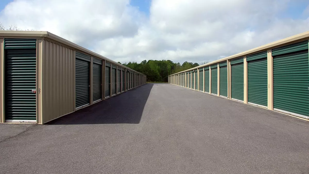 Row of green storage unit doors closed, with a clear paved road leading to the center of the image.