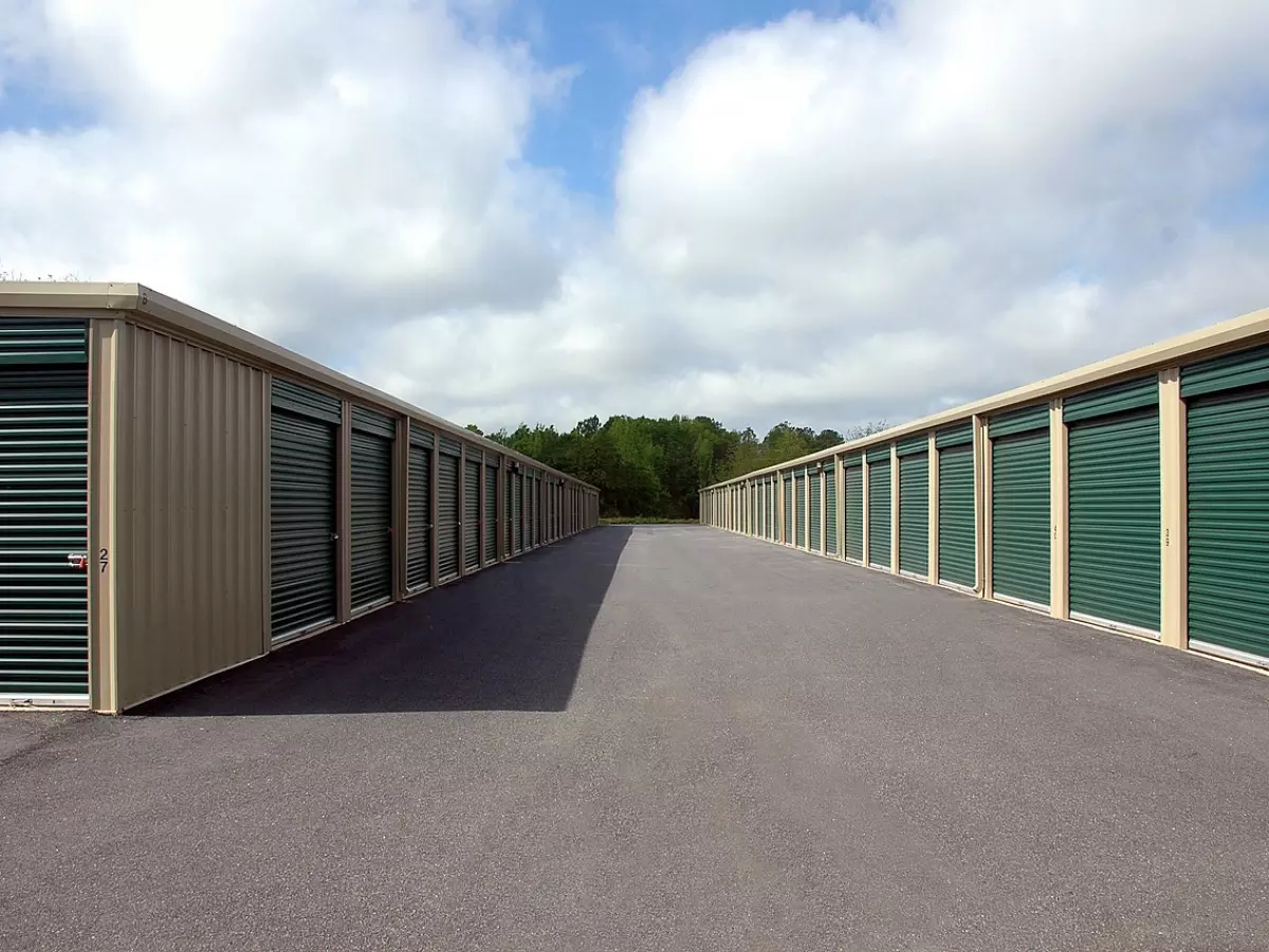 Row of green storage unit doors closed, with a clear paved road leading to the center of the image.