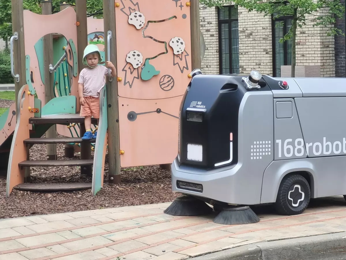 A close-up shot of a silver autonomous vehicle,  with the brand name '168Robotics' clearly visible. The vehicle is driving on a paved road, with some greenery in the background.