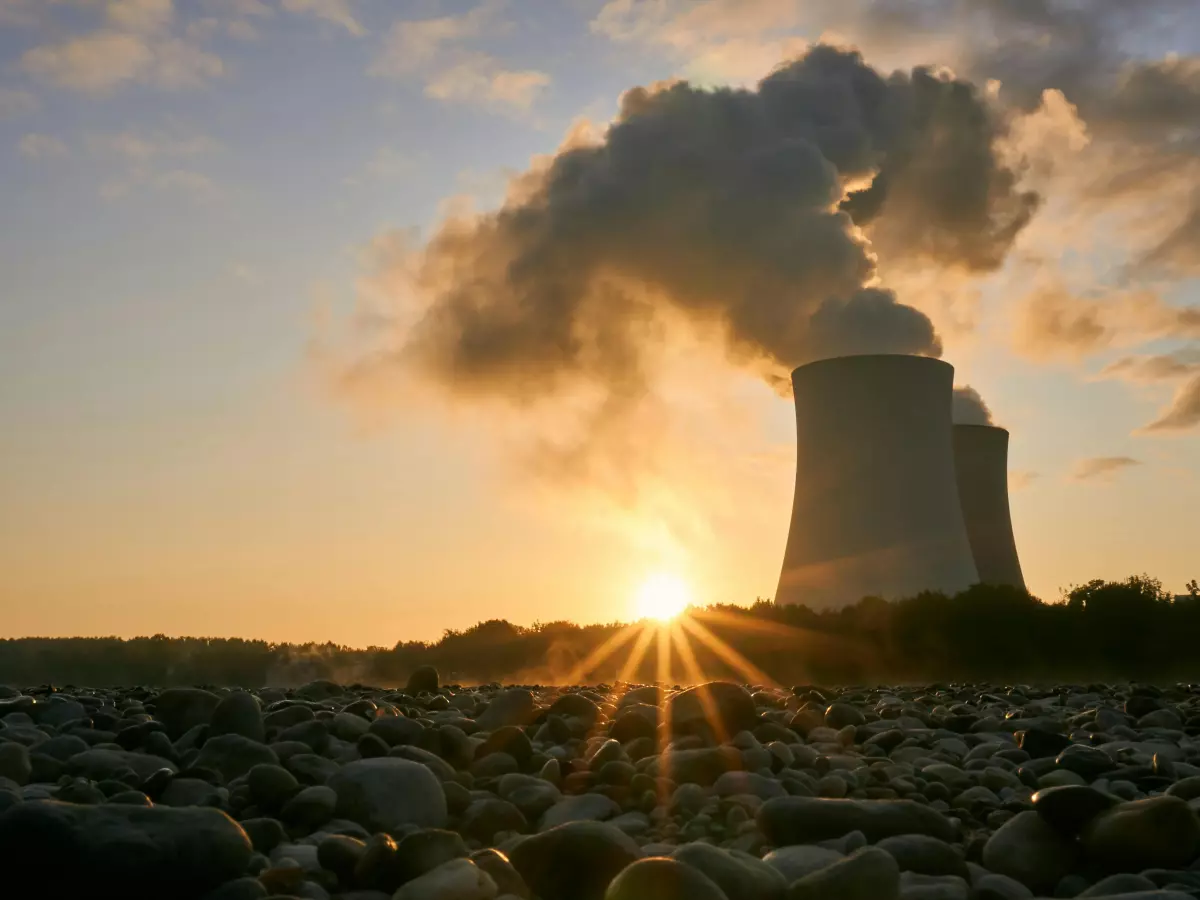 A nuclear power plant with steam billowing from its cooling towers at sunset.