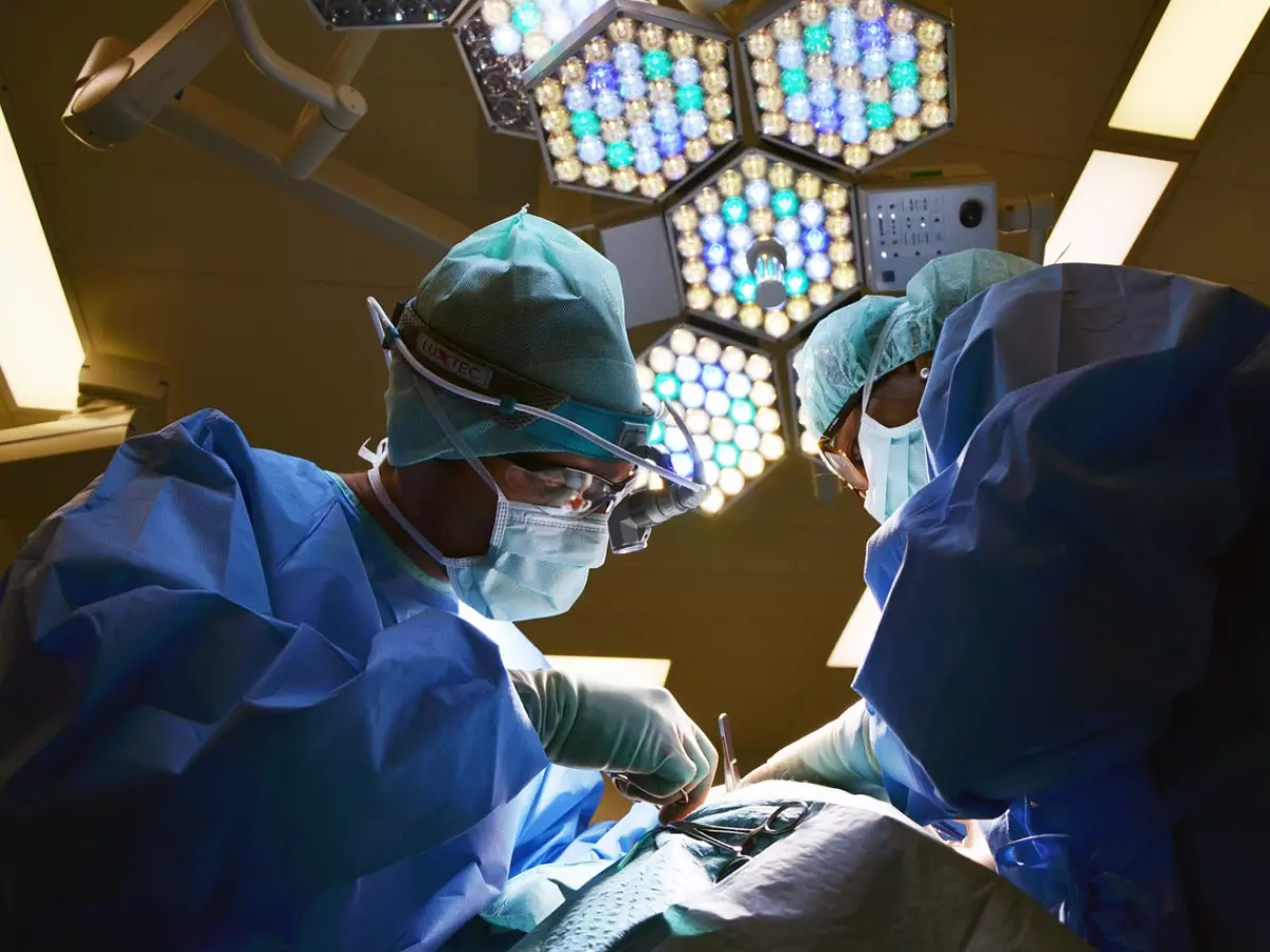 Two surgeons in blue scrubs operate on a patient in a dimly lit operating room