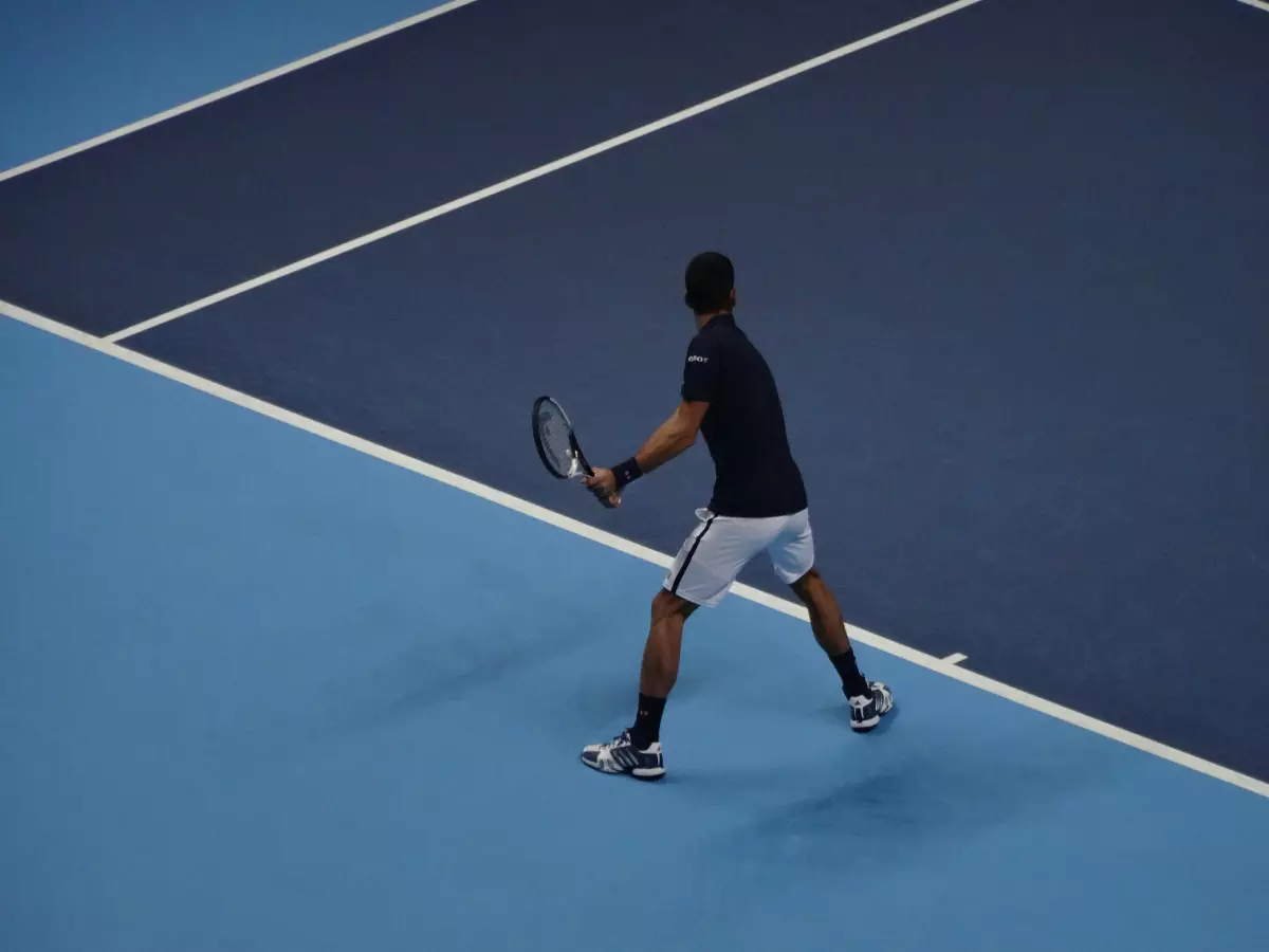 A tennis player mid-swing, hitting the ball with a focused expression. The image captures the motion of the swing with a blur, creating a sense of speed and action.