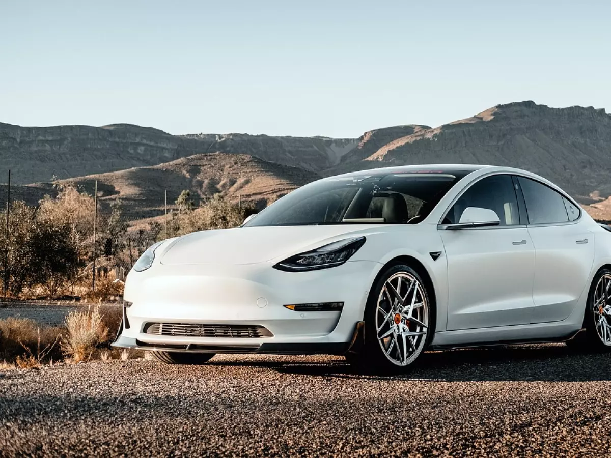 A white Tesla Model 3 parked in a desert landscape.