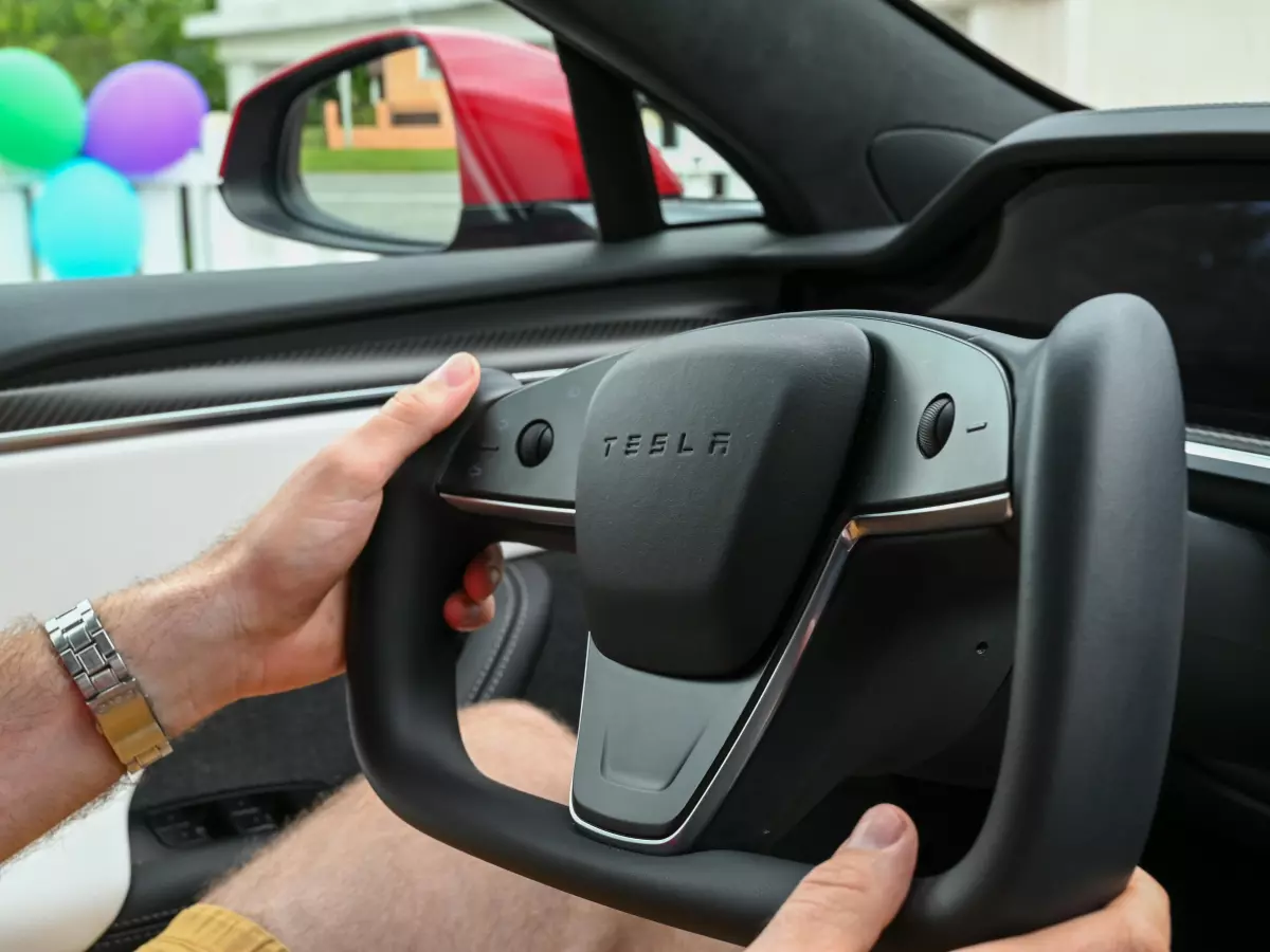 Close-up view of a person's hands on the steering wheel of a Tesla Model 3, showing the steering wheel design and interior.